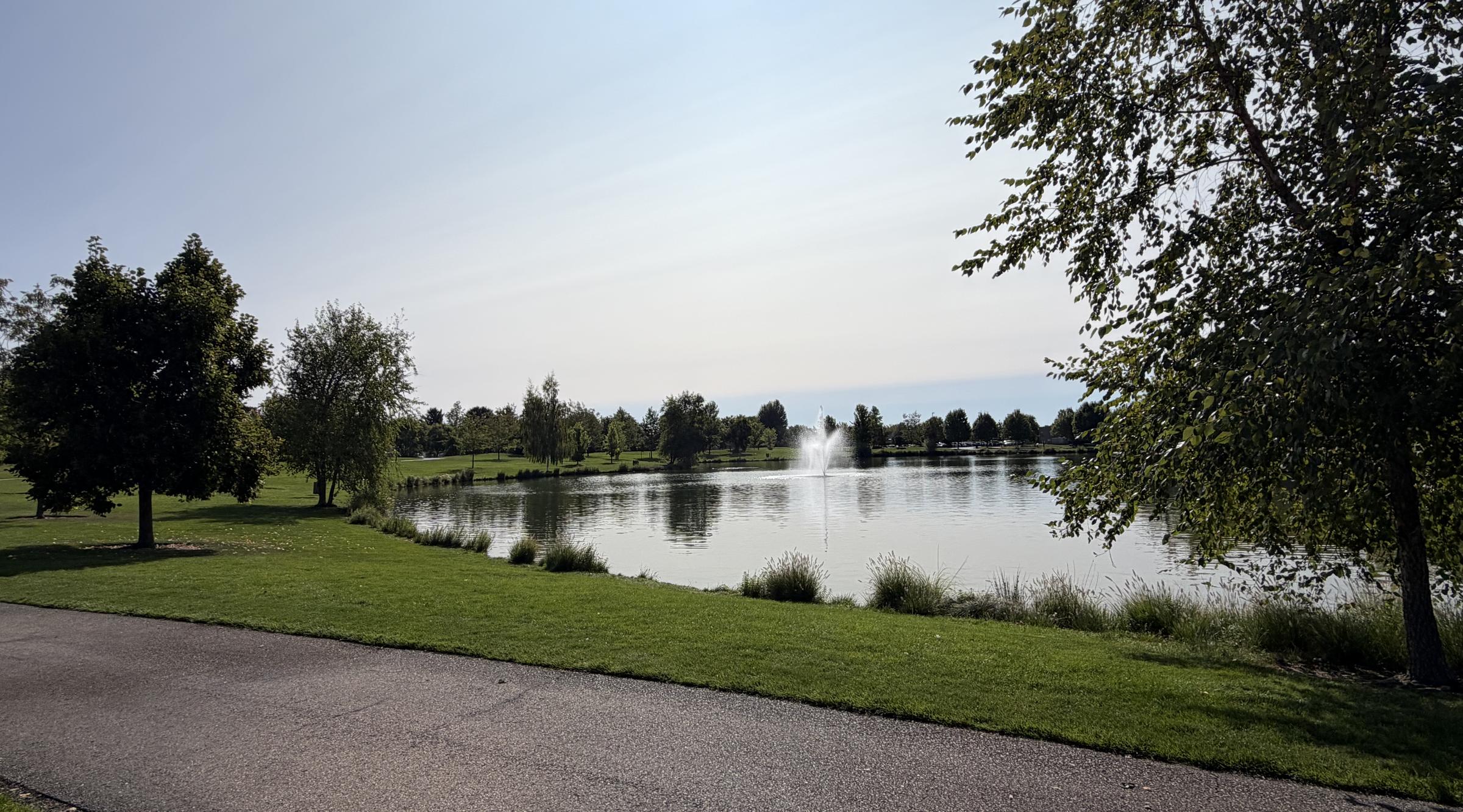 A lake with a fountain in a Meridian city park, mown lawns and trees along the path